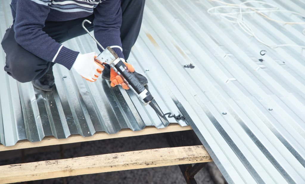 Worker using glue gun with adhesive to fix the metal steel on the roof.